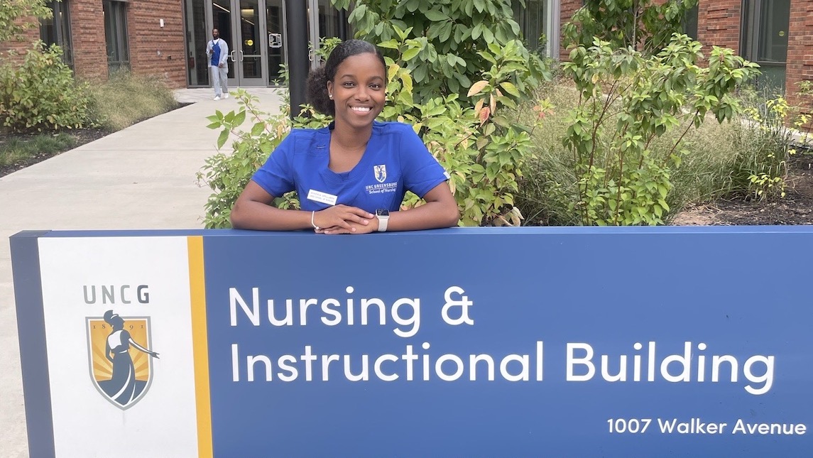 UNCG SON Alumna Nykeria Spellmon in front of the Nursing Instructional Building sign.