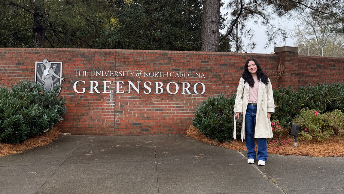 Mirian Dias, a visiting Fulbright Scholar from Brazil, stands in front of the UNCG sign.