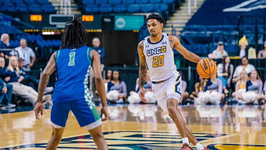 UNCG basketball player comes down the court towards a defender.