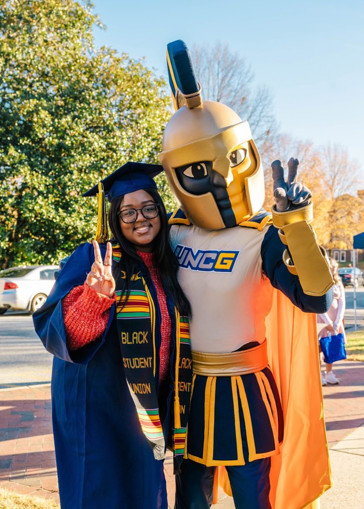 UNCG graduate in cap and gown poses with Spiro