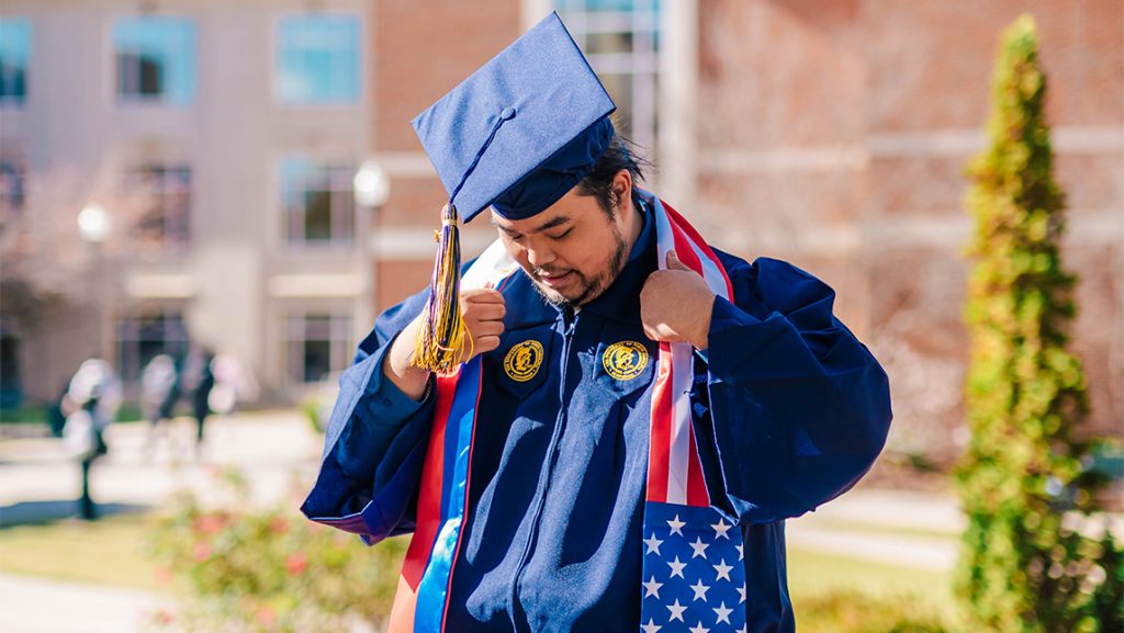 Elijah Resuello adjusts a stole over his UNCG graduation gown.