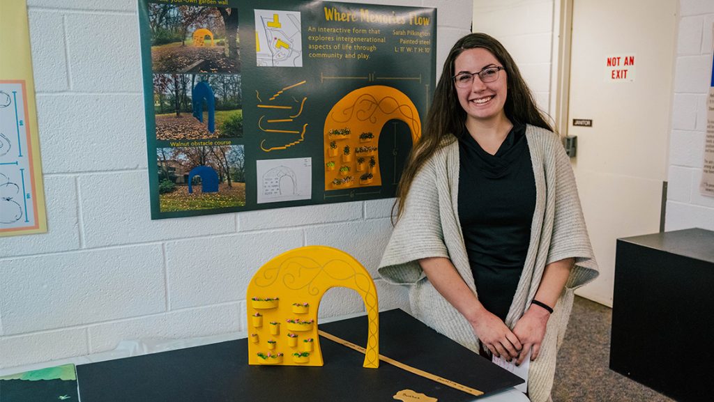 A UNCG student stands next to her model of a sculpture about movement.