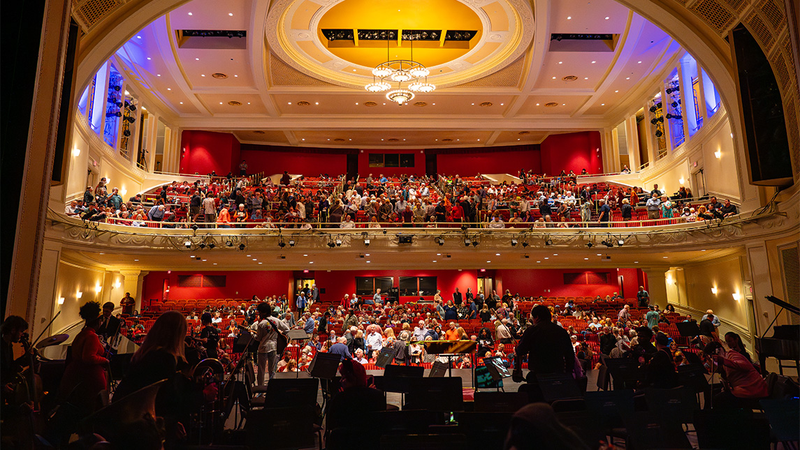 A view of the UNCG Auditorium gallery from the stage filled with an orchestra.