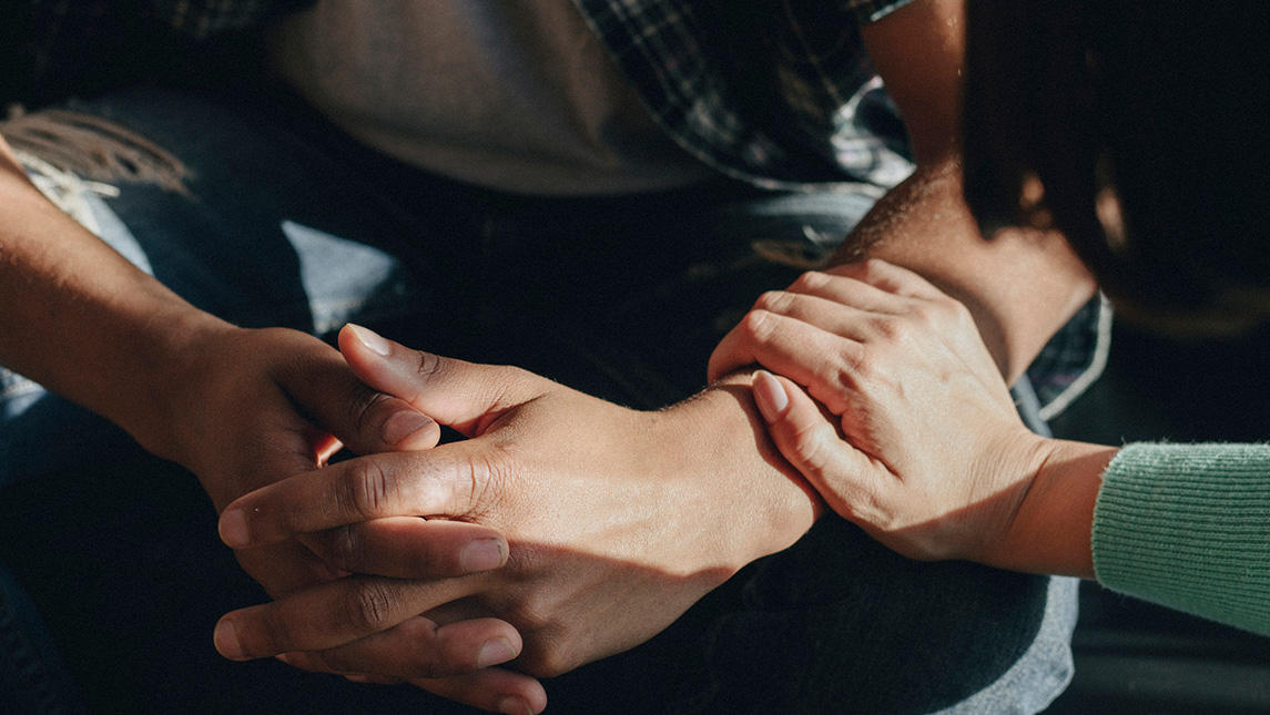 Close-up on a woman placing her hand comfortingly on a teenage boy's arm.