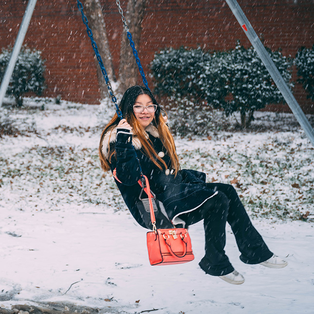 Student swings on campus in the snow.