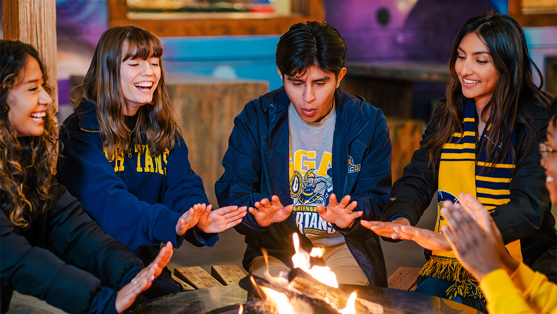 A group of UNCG students circle around a fire pit.