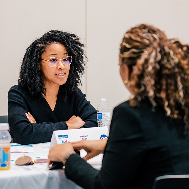 Two women talk at a table interview-style.