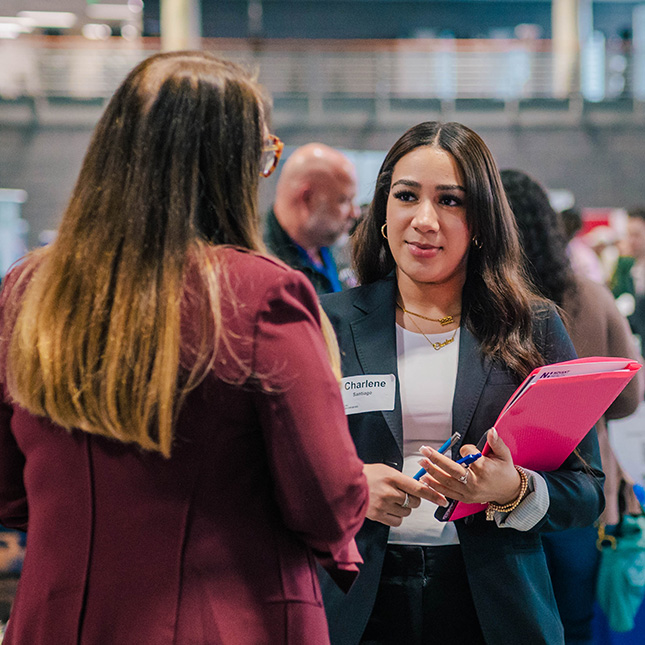 Student in business suit with nametag and portfolio talks with an employer.