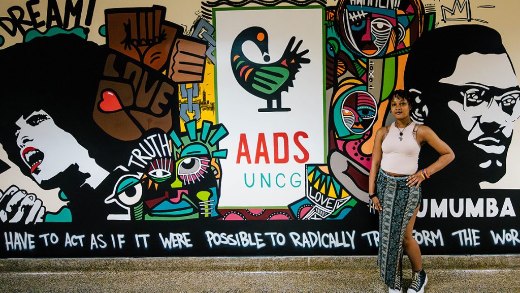 Student stands in front of a mural in a hallway.