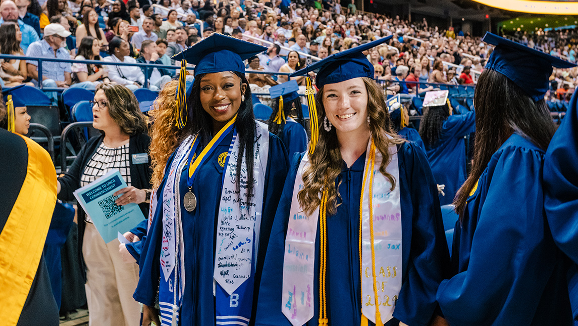 Two UNCG grads smile in their caps and gowns.