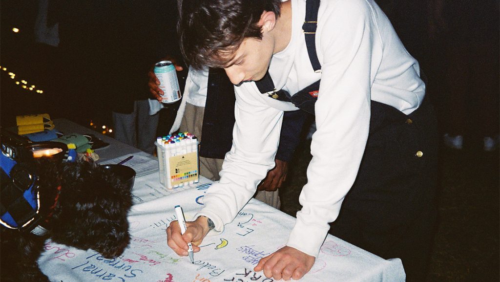 A student signs a large sheet of paper full of messages.