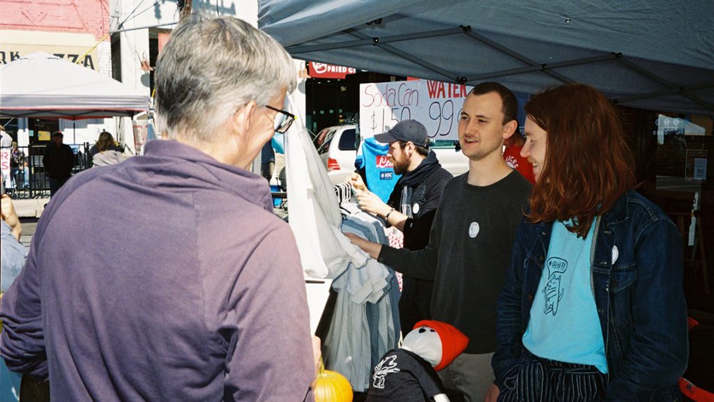 UNCG students talk with a Greensboro resident under a tent downtown.