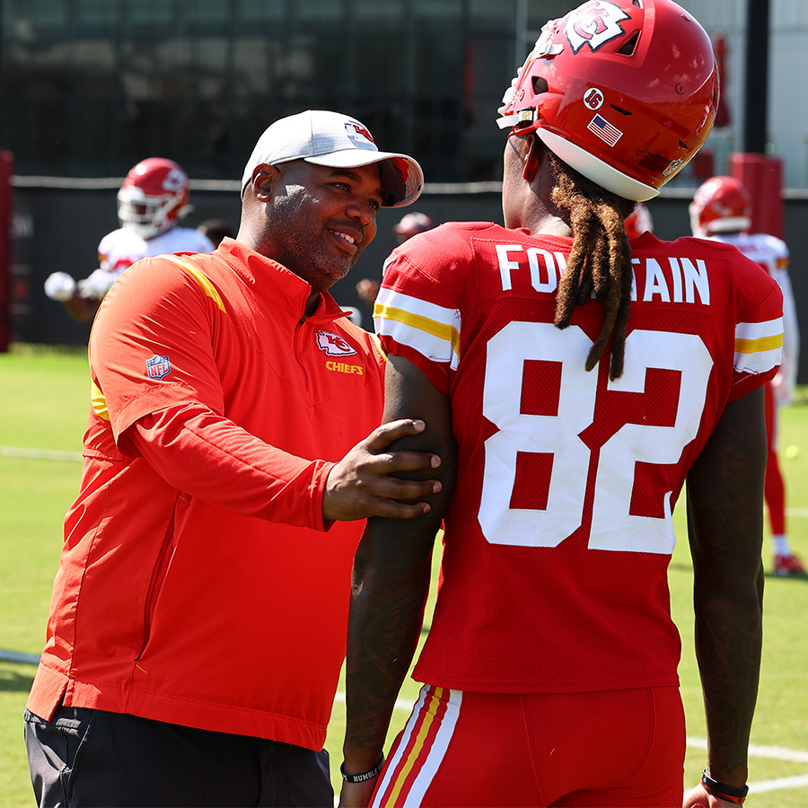 UNCG alum Dr. Shaun Tyrance talks to a Kansas City Chiefs player on the field.