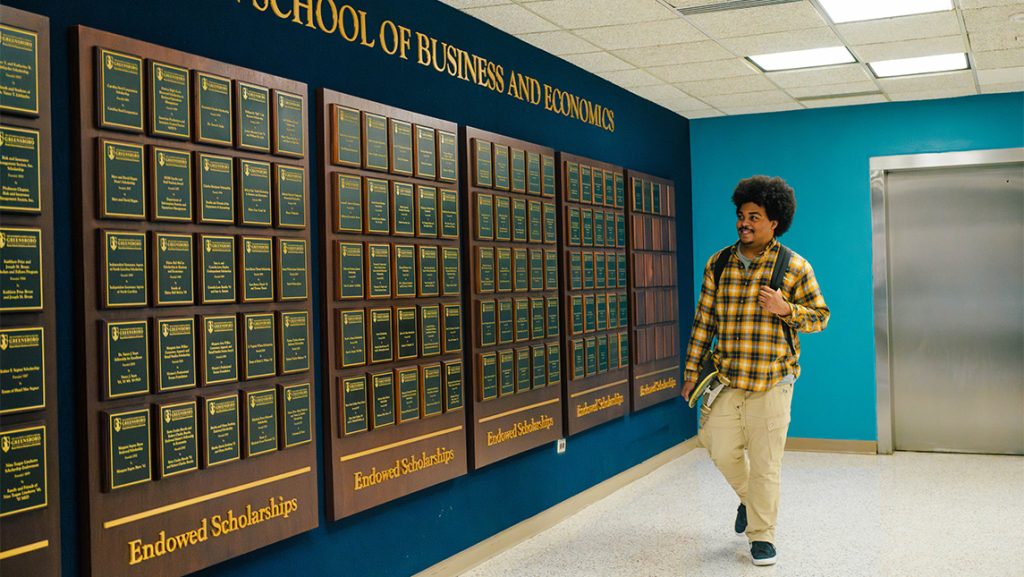 UNCG student Taylee Gaillard walks past plaques on the wall of the Bryan School.