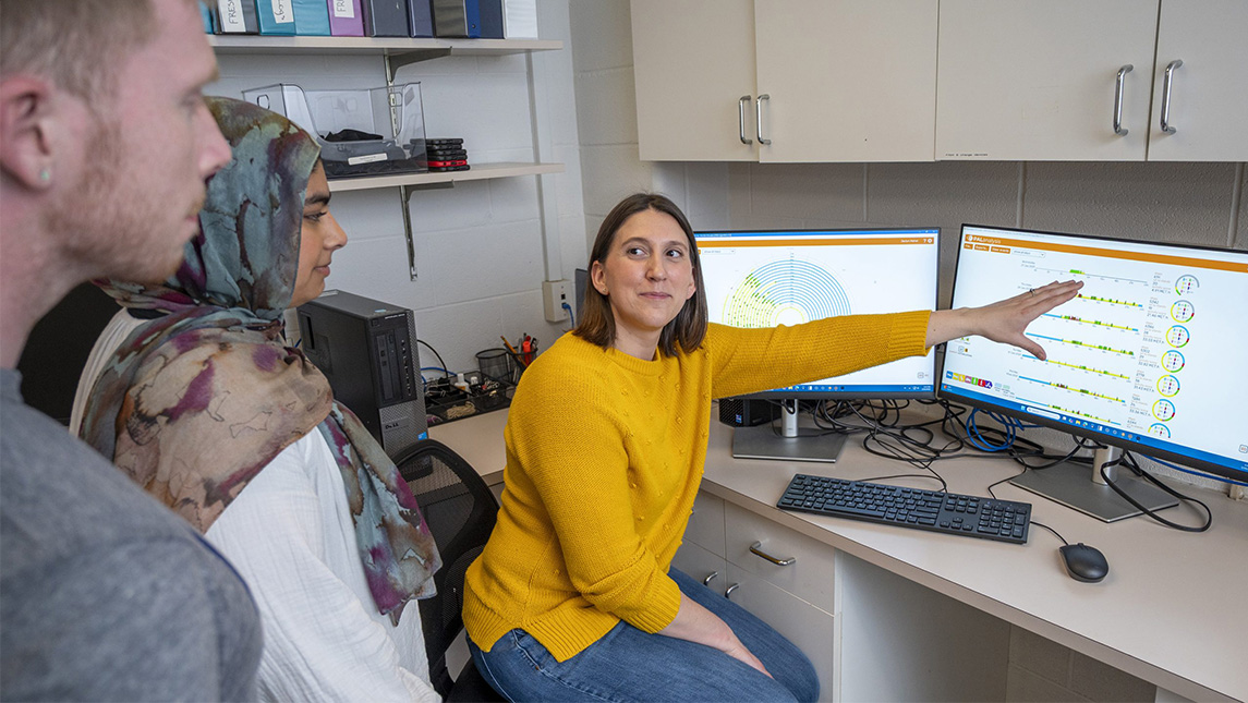 UNCG's Dr. Jaclyn Maher points at a computer while students watch.